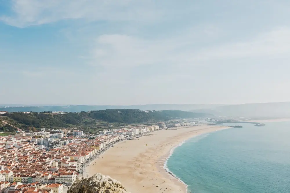 Vista panorâmica sobre a Nazaré, com a vila, a extensa praia e a costa atlântica vistas do alto.
