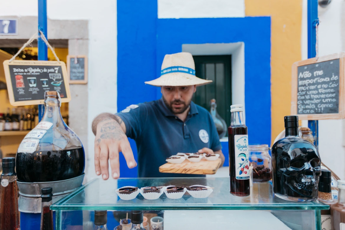 Funcionário serve ginja tradicional de Óbidos em copos de chocolate numa loja típica da vila medieval, uma das experiências gastronómicas mais emblemáticas de Portugal.