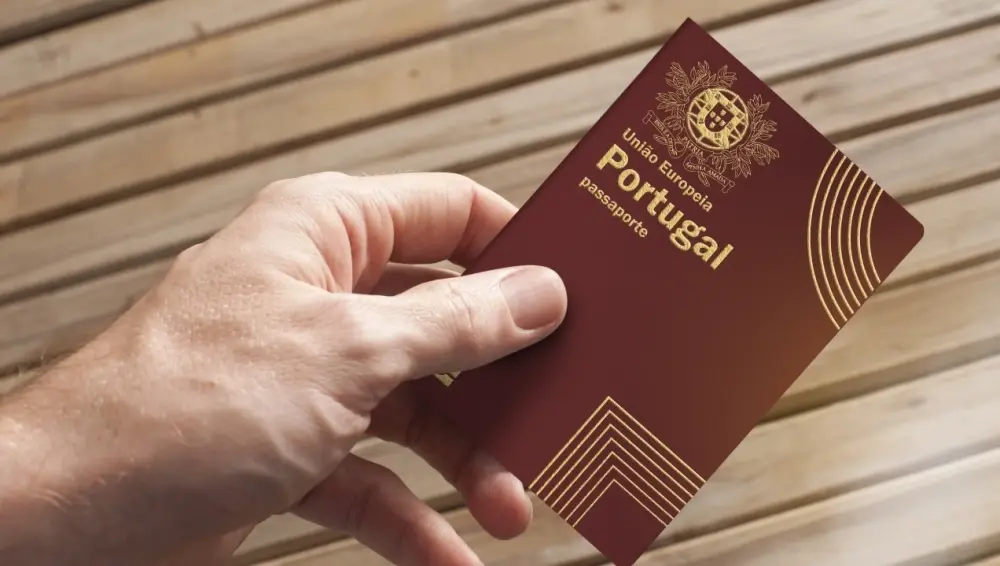 Portuguese passport held in one hand against a wooden background.