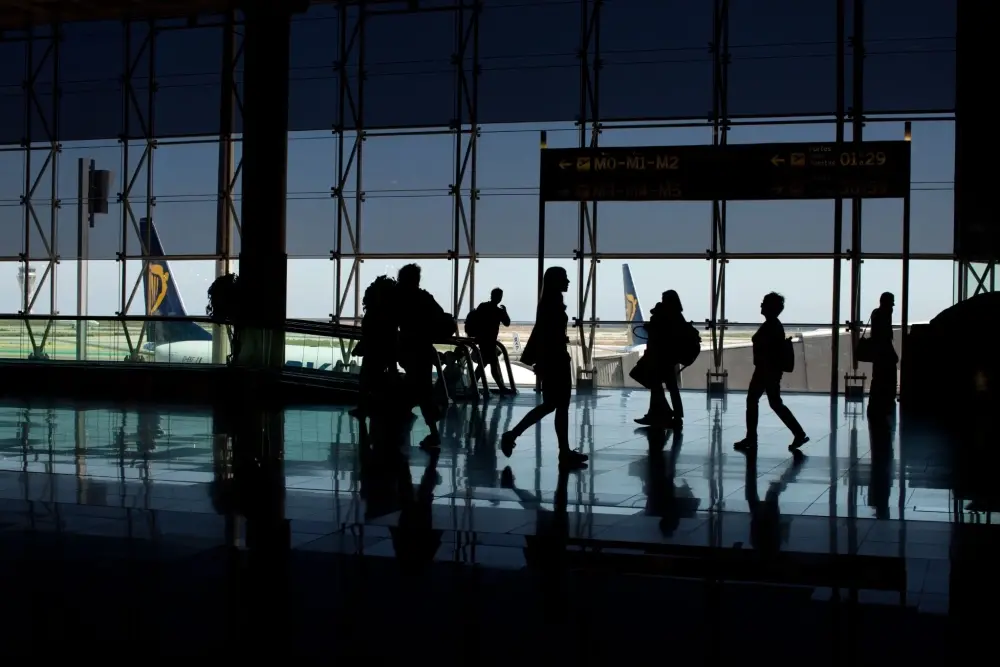 Travellers walking through an airport terminal with aircraft visible through large windows at Lisbon Airport.