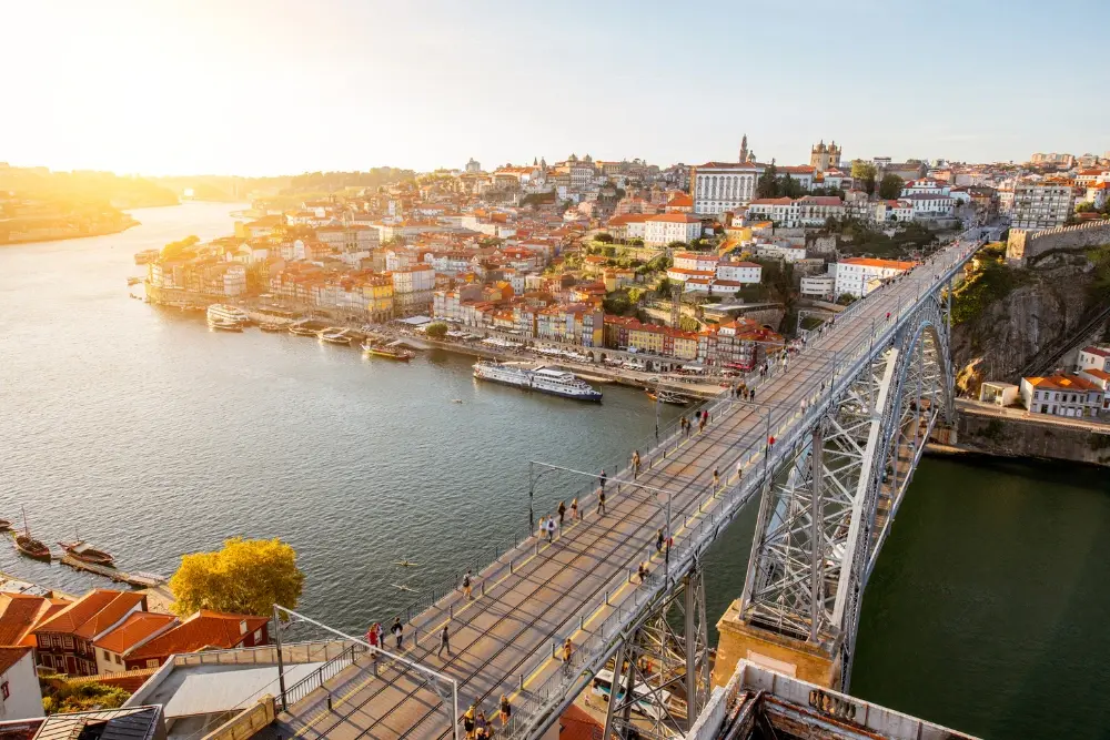 Dom Luís I Bridge crossing the Douro River at sunset, with Porto’s historic centre and Ribeira waterfront beyond.