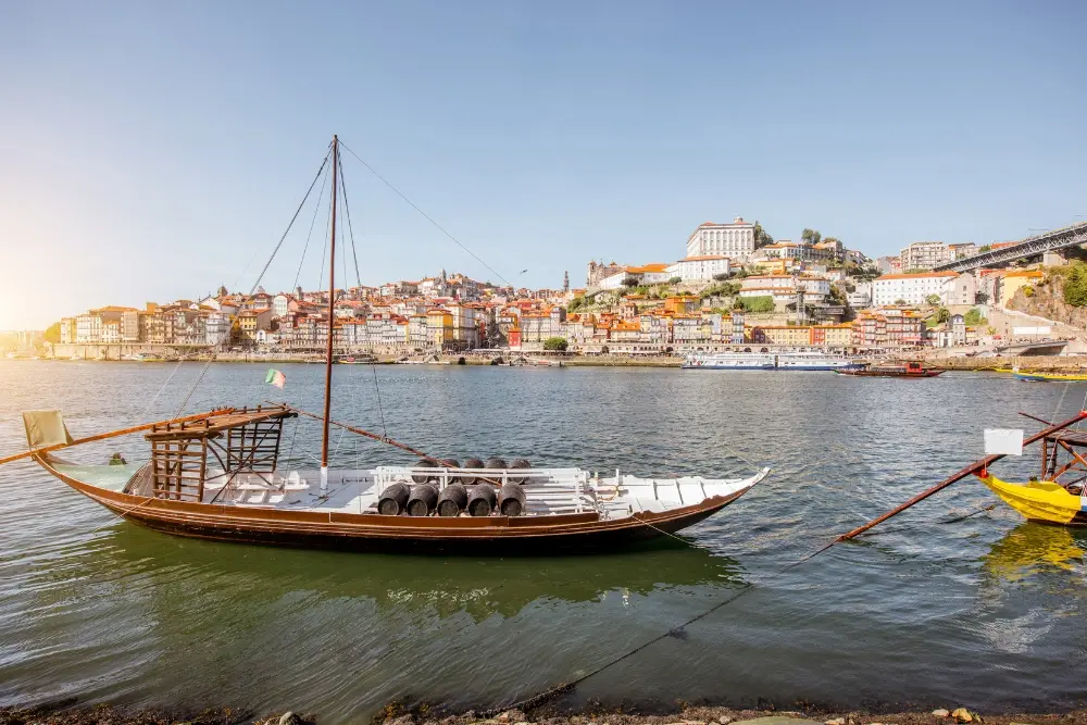 Traditional rabelo boat on the Douro River with Porto’s Ribeira waterfront and historic cityscape in the background.