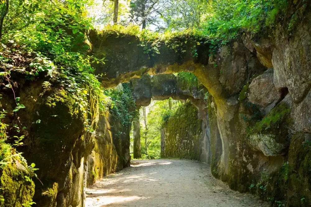 Ponte de pedra e caminho arborizado nos jardins exuberantes da Quinta da Regaleira em Sintra, Portugal