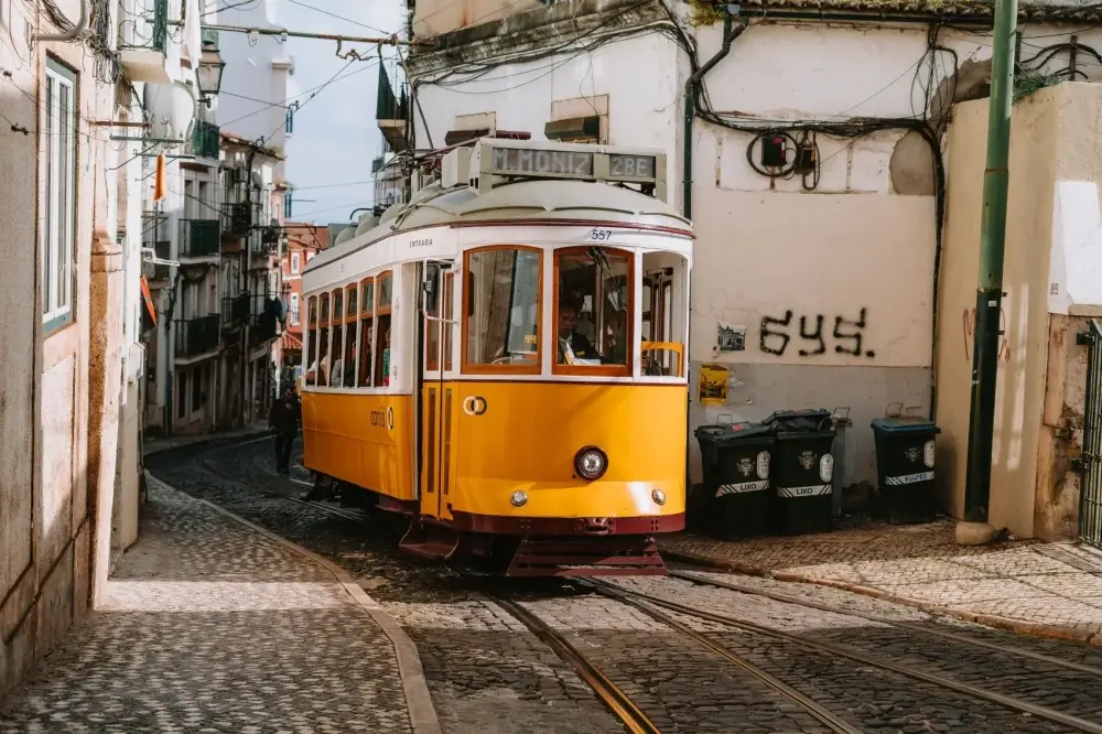 Elétrico 28 amarelo percorre uma rua estreita e empedrada de Alfama, em Lisboa, em direção ao Martim Moniz.