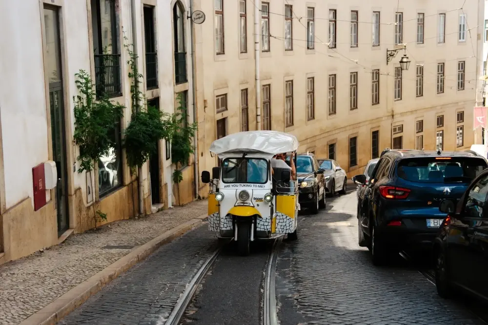 Tuk tuk percorre uma rua histórica de Lisboa junto aos carris do elétrico e a edifícios tradicionais.