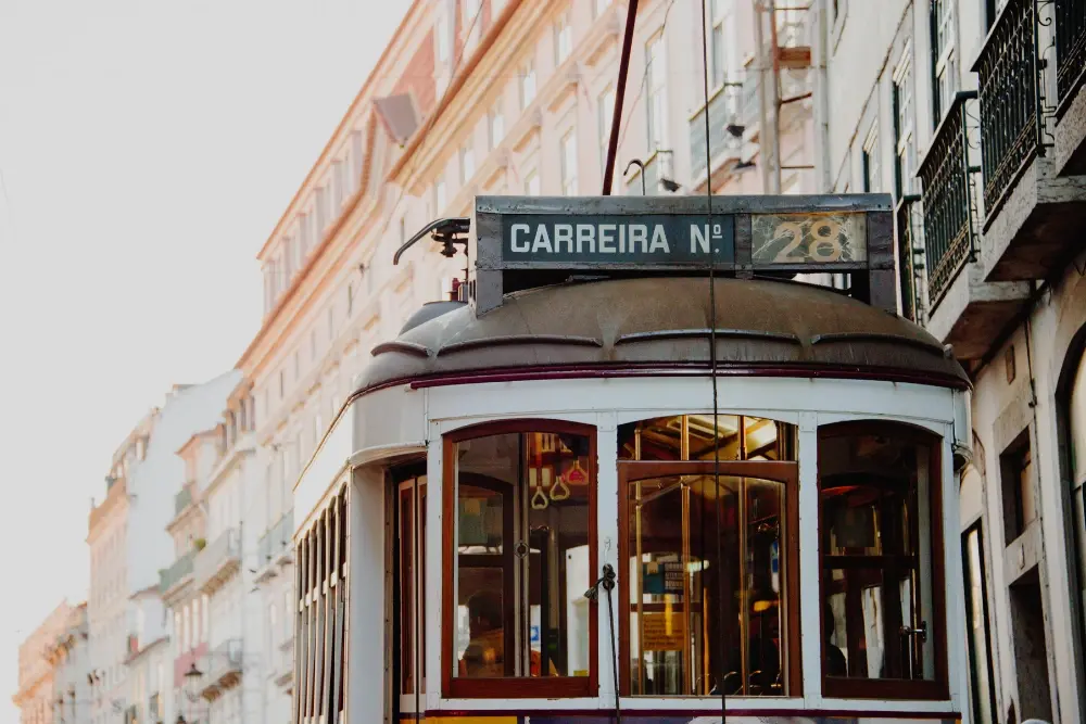 Vista aproximada do Elétrico 28 de Lisboa a circular por uma rua histórica ladeada por edifícios tradicionais.